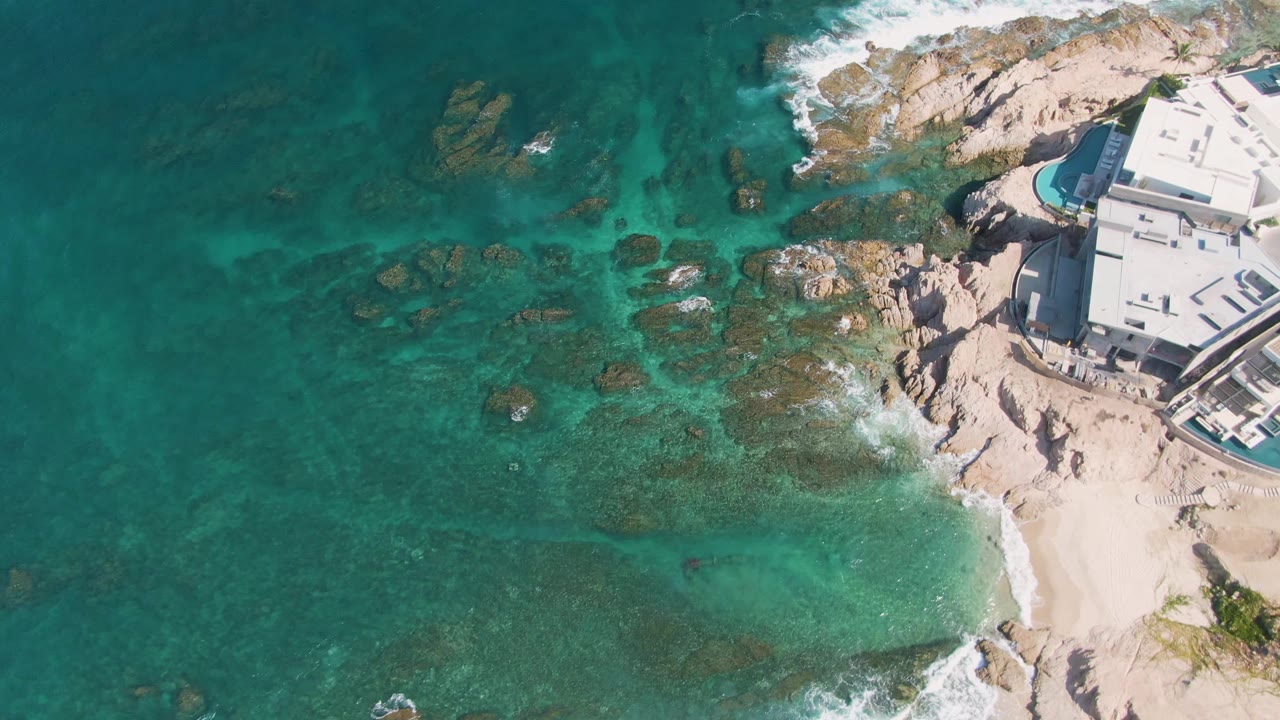 Clear ocean water and submerged rocks beside a rocky shore and building.
