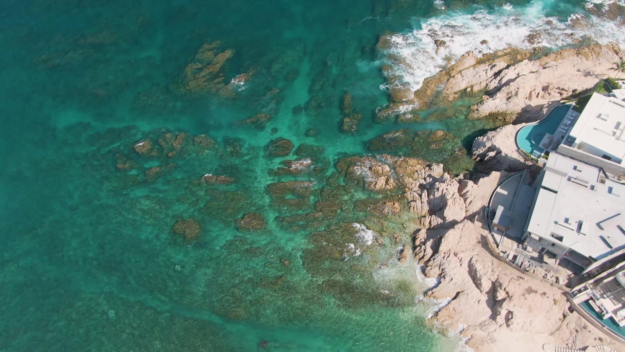 Aerial view of turquoise water, rocky shore, and a white coastal building.