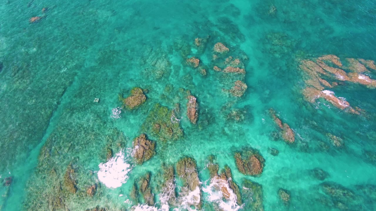 Top-down turquoise water over rocks and reef patches