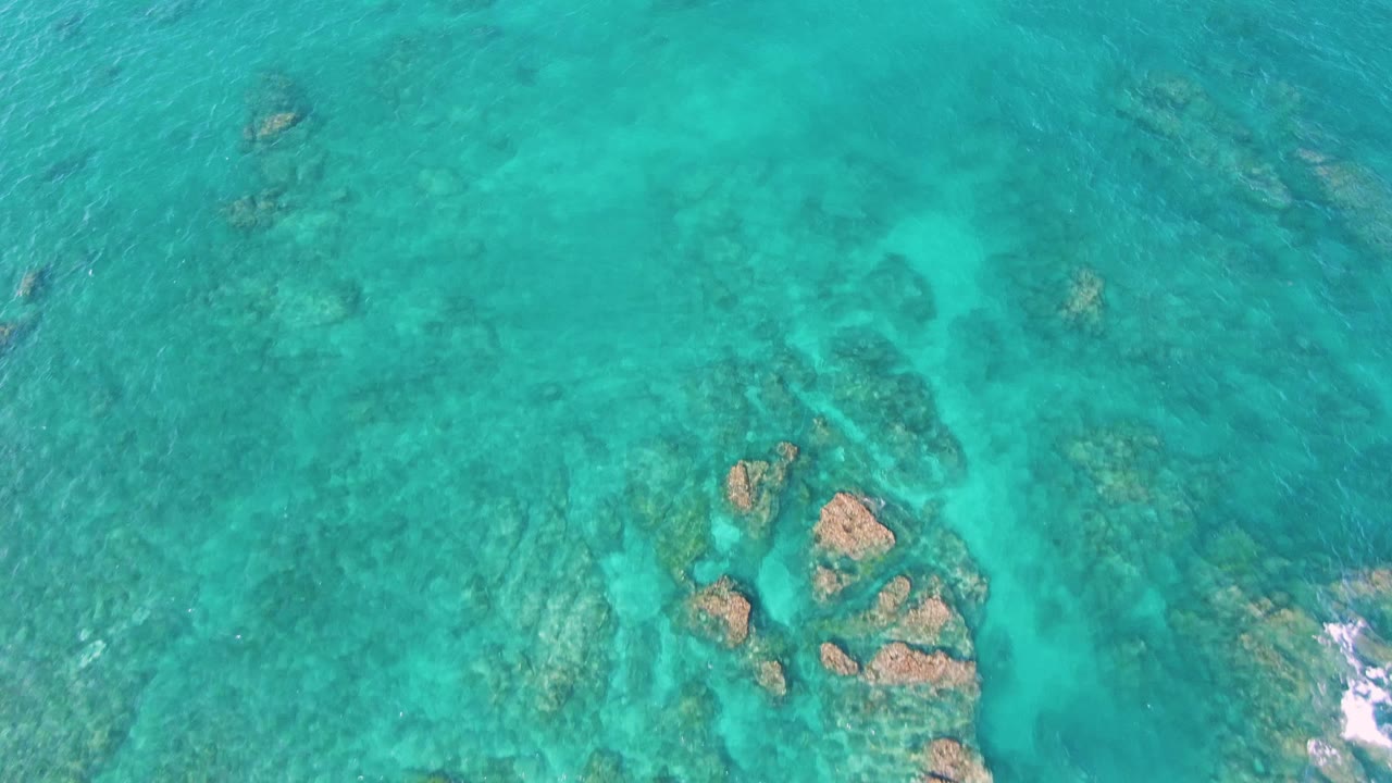 Straight-down view of turquoise water over submerged rocks and sandy seabed at El Tule Beach, Los Cabos, with no visible people.