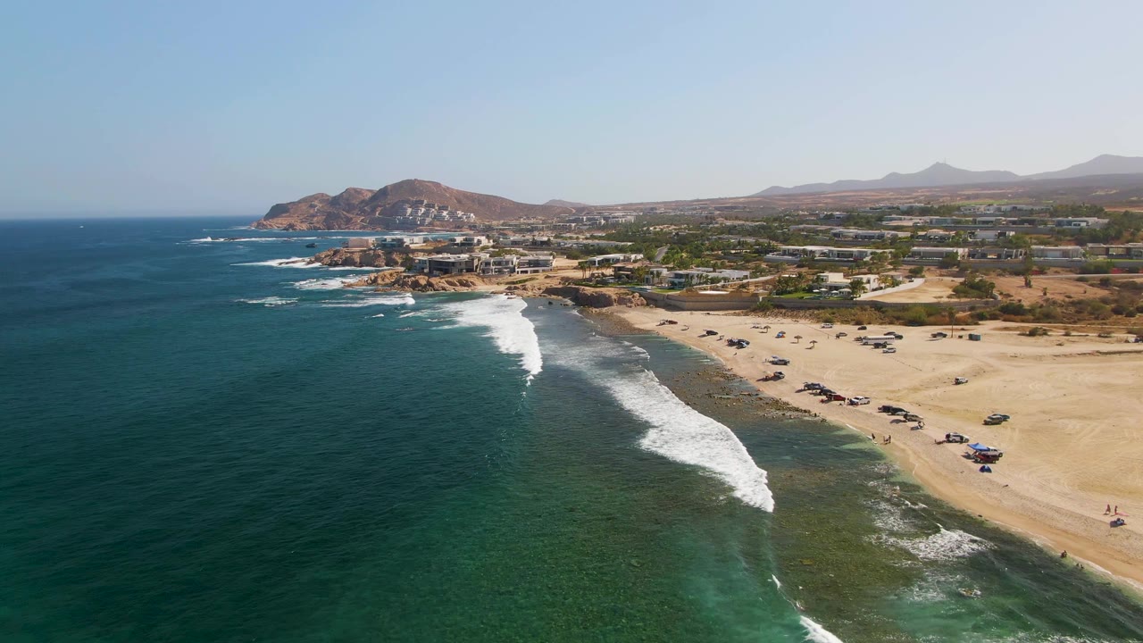 White surf rolls toward a sandy beach with parked vehicles.