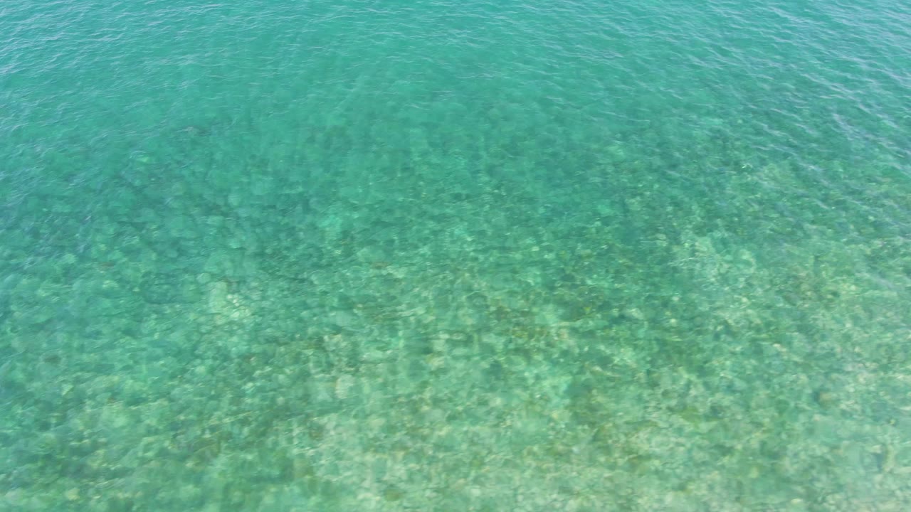 Transparent turquoise sea at El Tule Beach in Los Cabos reveals a pale sandy bottom with scattered darker seabed areas and no visible people.