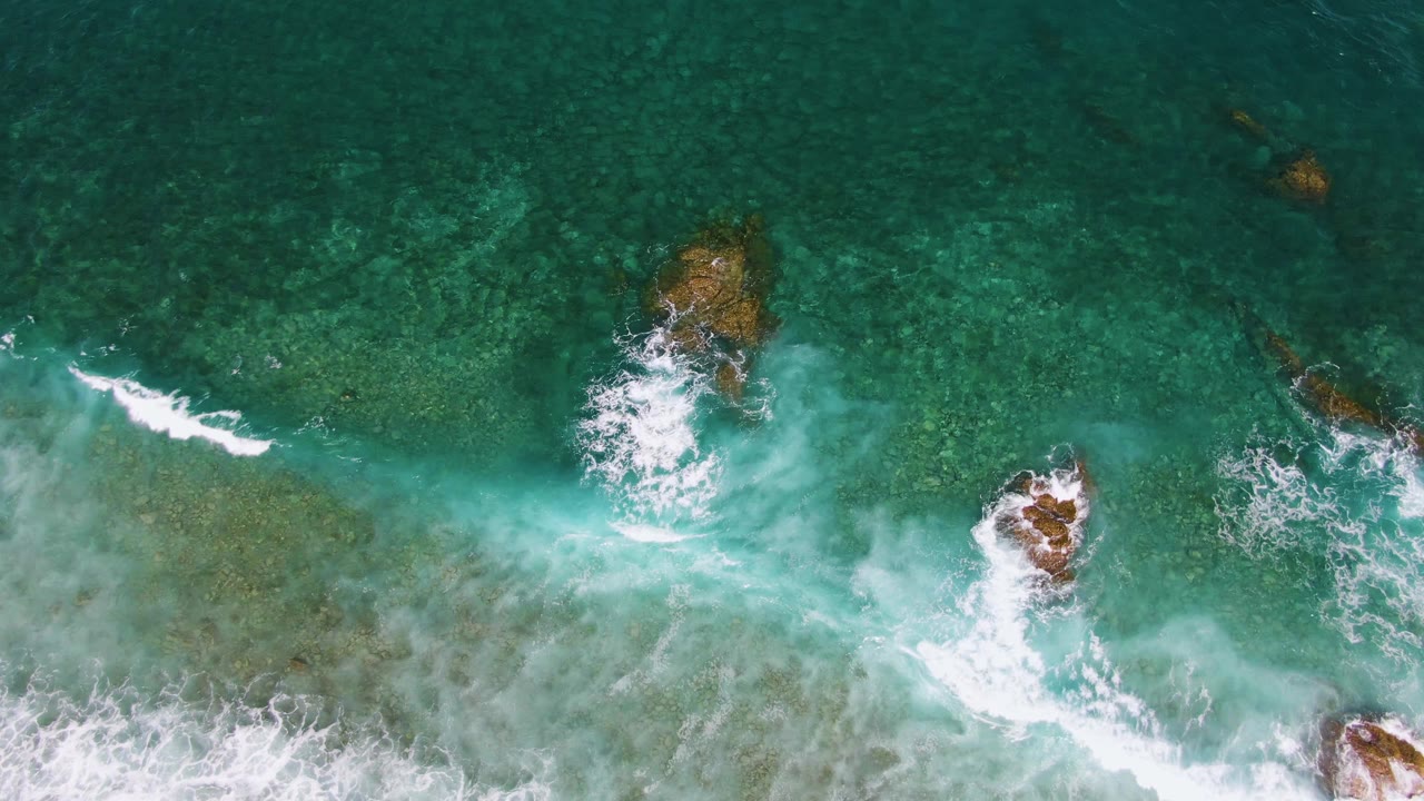 Overhead turquoise ocean water with white surf and submerged rocks.