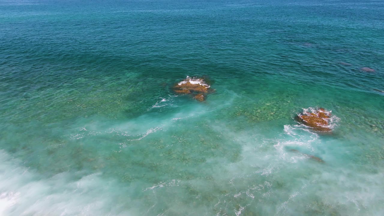 Breaking wave foam pushes across shallow turquoise water near rocks