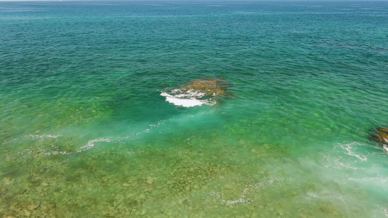 Rocky outcrop in clear turquoise ocean with white wave foam