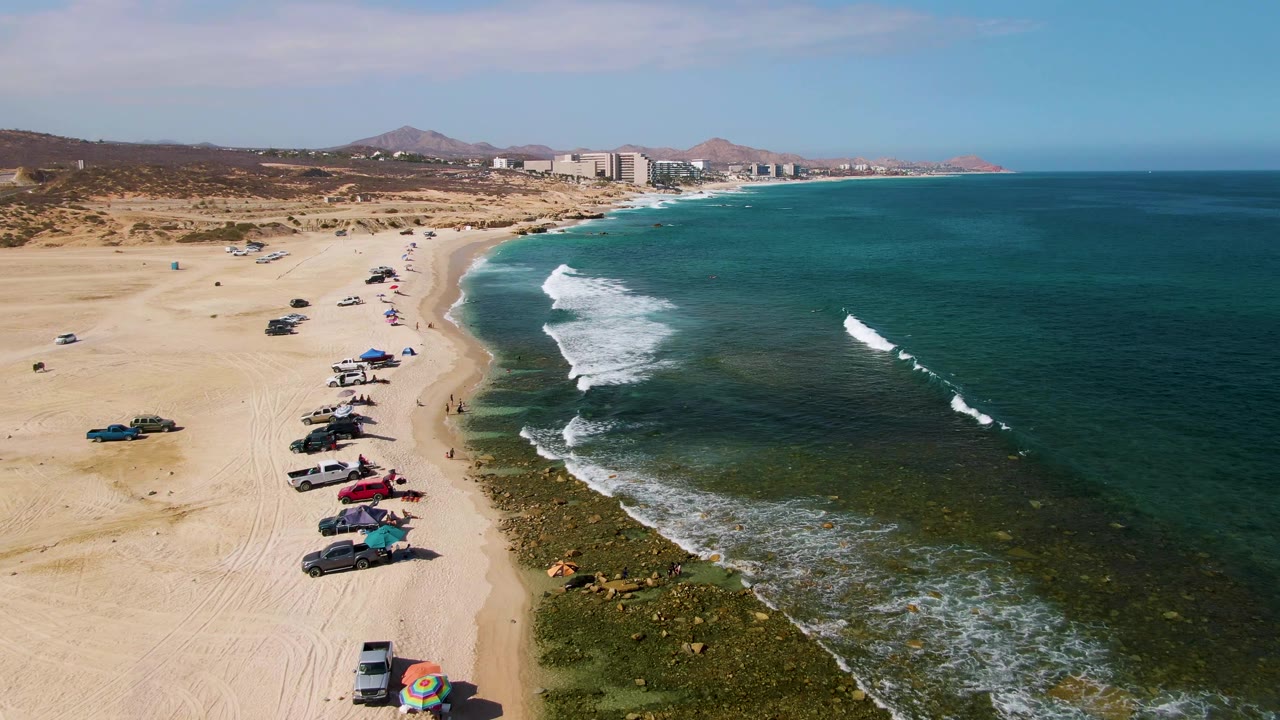 Beach parking line beside foamy waves and distant buildings.