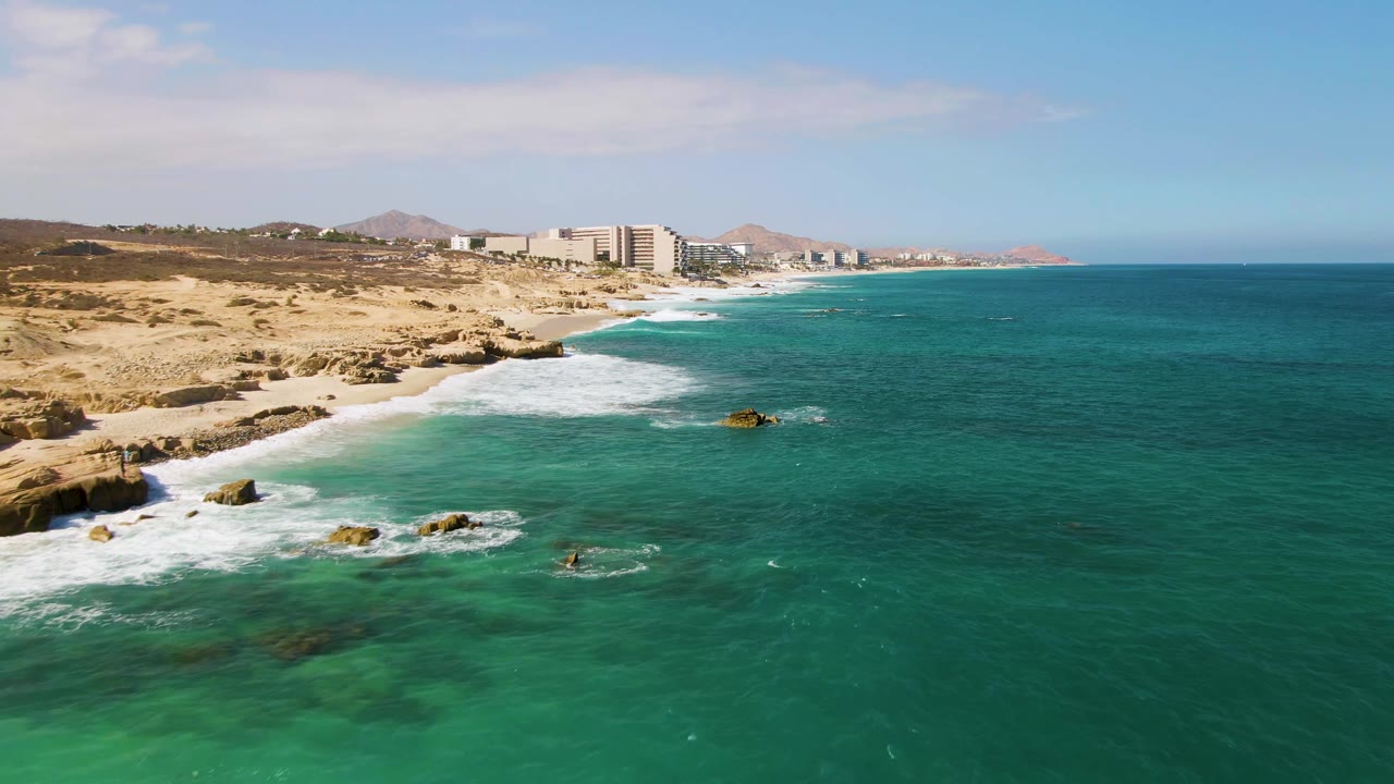 Aerial view of turquoise ocean waves breaking on a rocky sandy coastline.