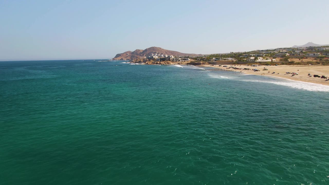 Aerial view of turquoise ocean beside a sandy beach and distant hills.
