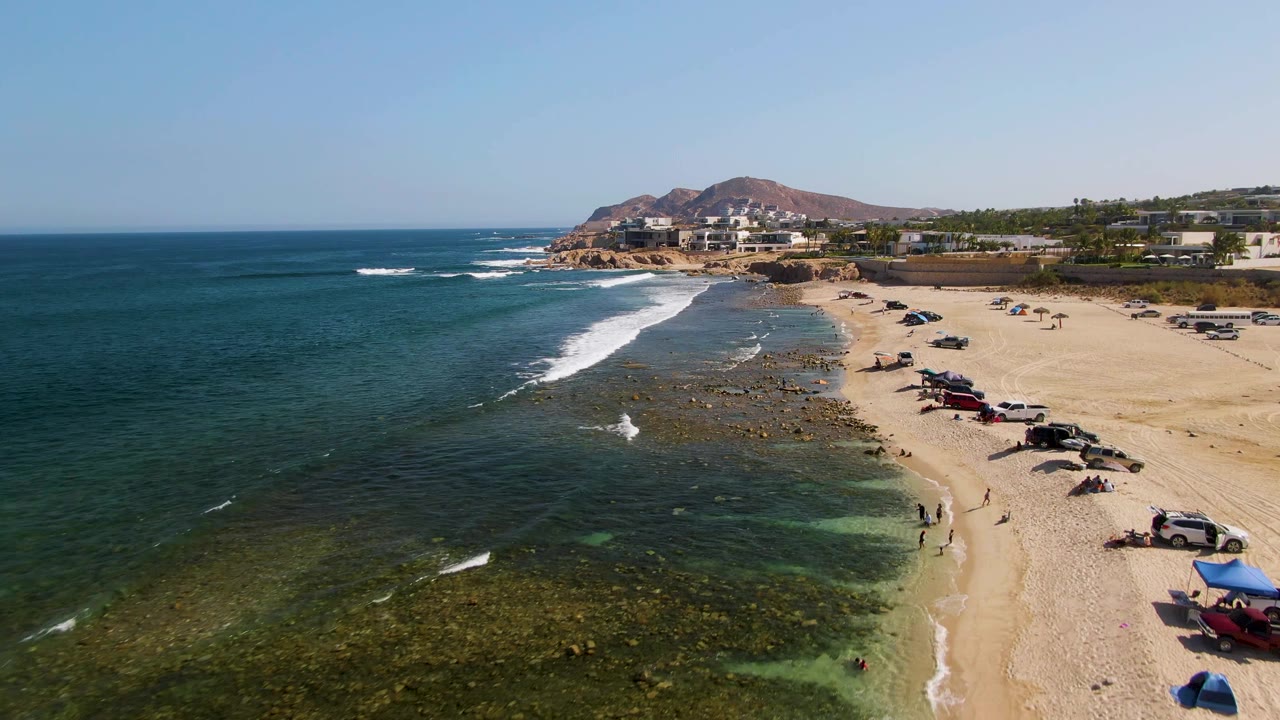 Drone view of green shallows beside a sandy beach with vehicles
