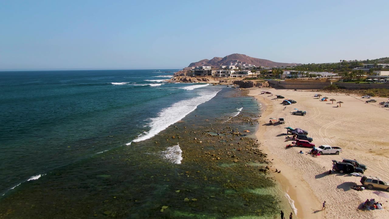 Wide beach aerial with surf sweeping toward parked vehicles