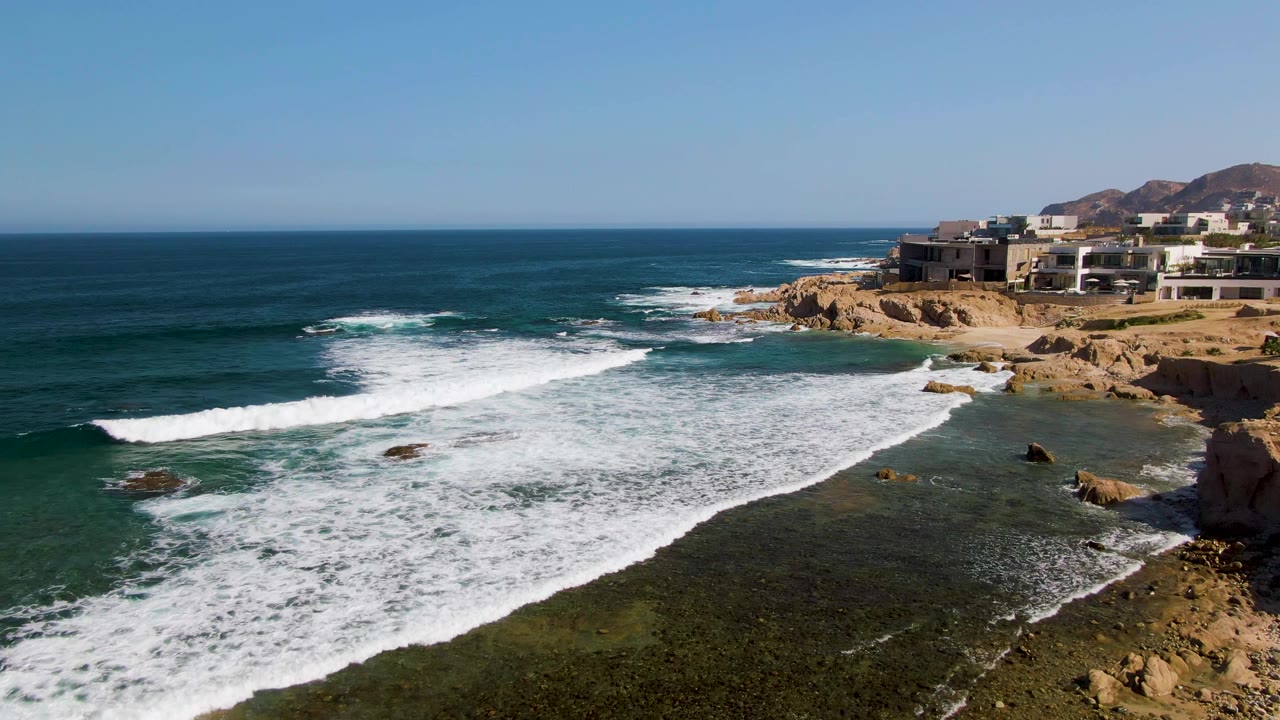 Foam covers more of the rocky shallows as waves break below a clear horizon.
