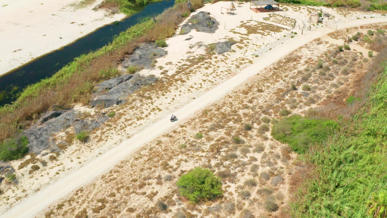 Aerial view of a small vehicle on a sandy dirt road beside a narrow waterway.