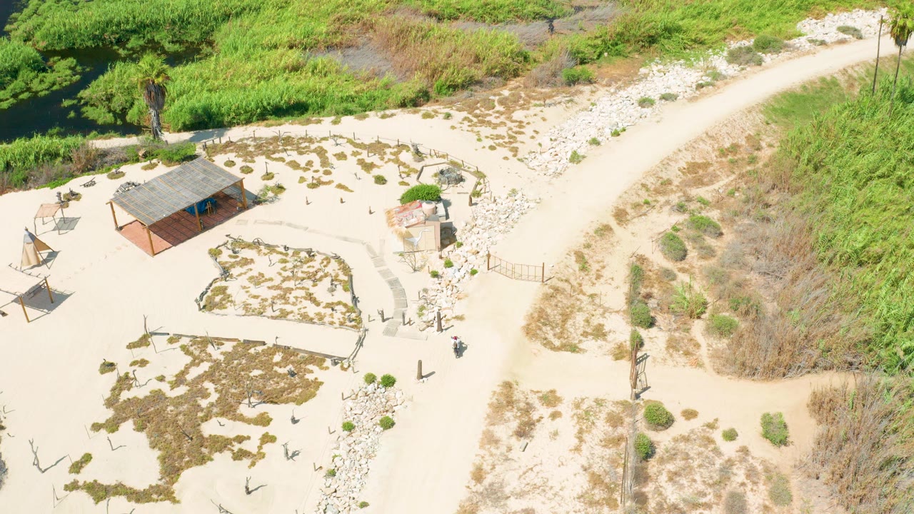 High aerial view of a rural sandy clearing with a path, small building, and vegetation.
