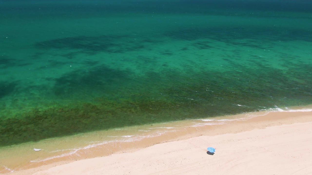 High aerial view at Playa Miramar Los Cabos with the water filling most of the frame, a diagonal surf line along the sand, and no visible people.