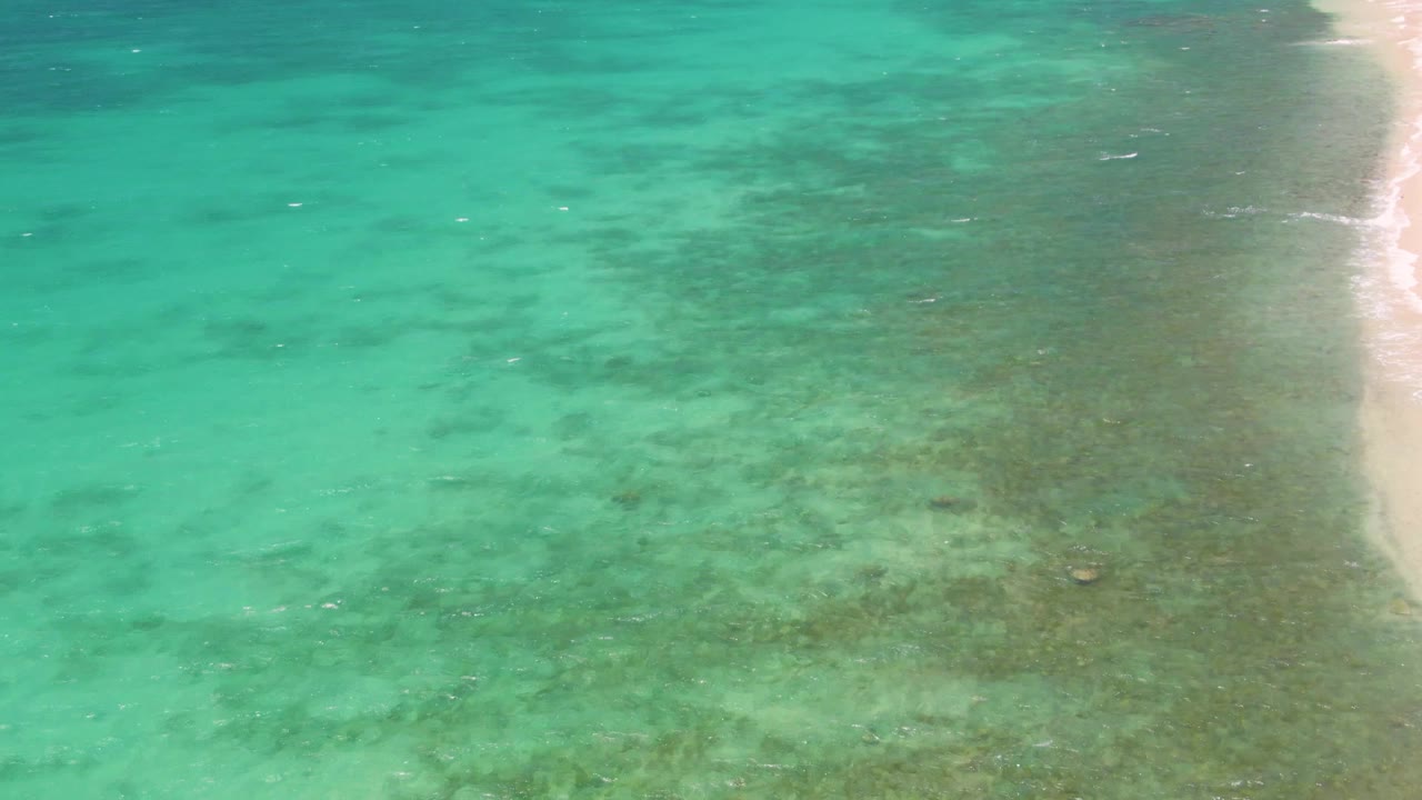 Clear green-blue water with foam along the beach edge.
