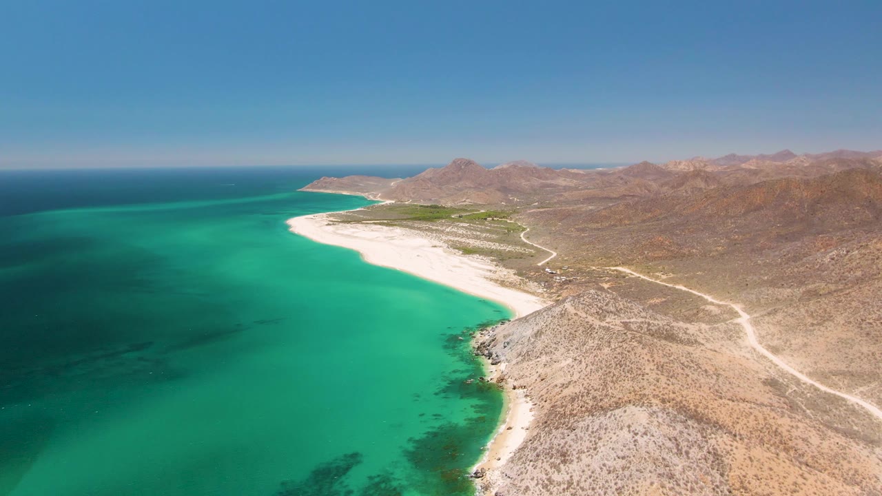 Oblique aerial of a white sand beach bordered by turquoise ocean and rocky terrain.