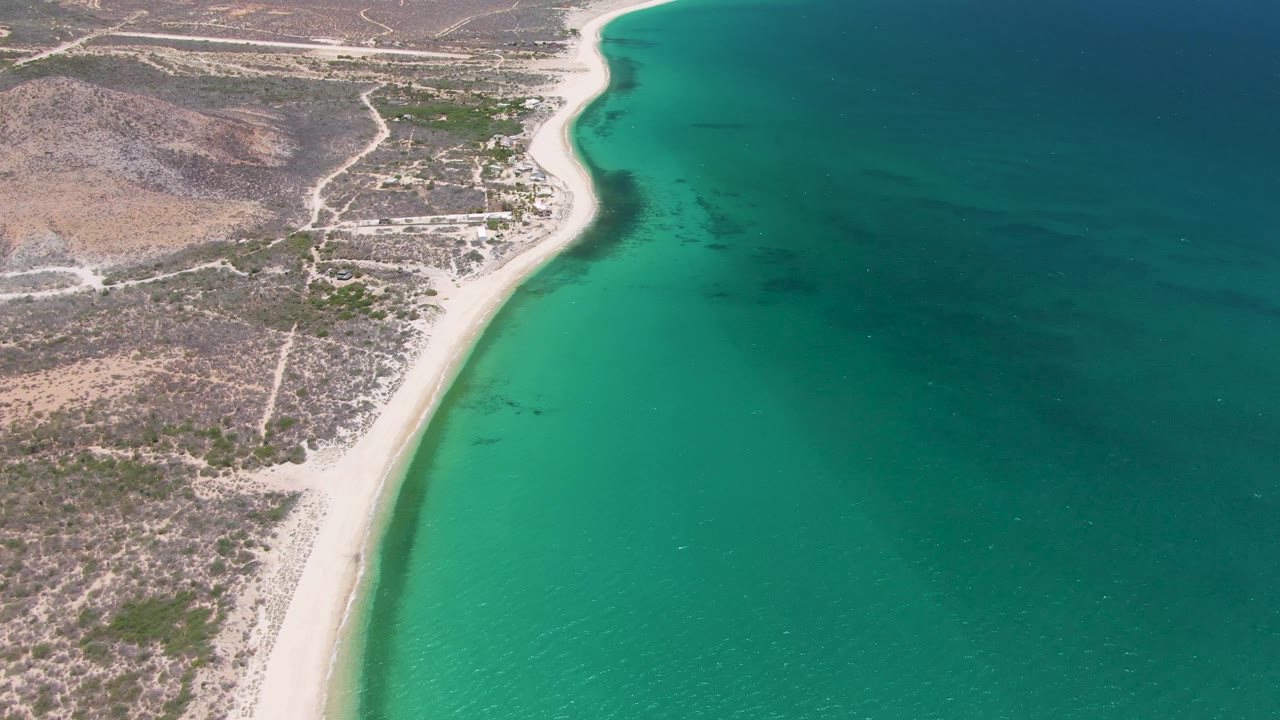 Aerial view of a sandy shoreline beside turquoise ocean water and dry coastal land.