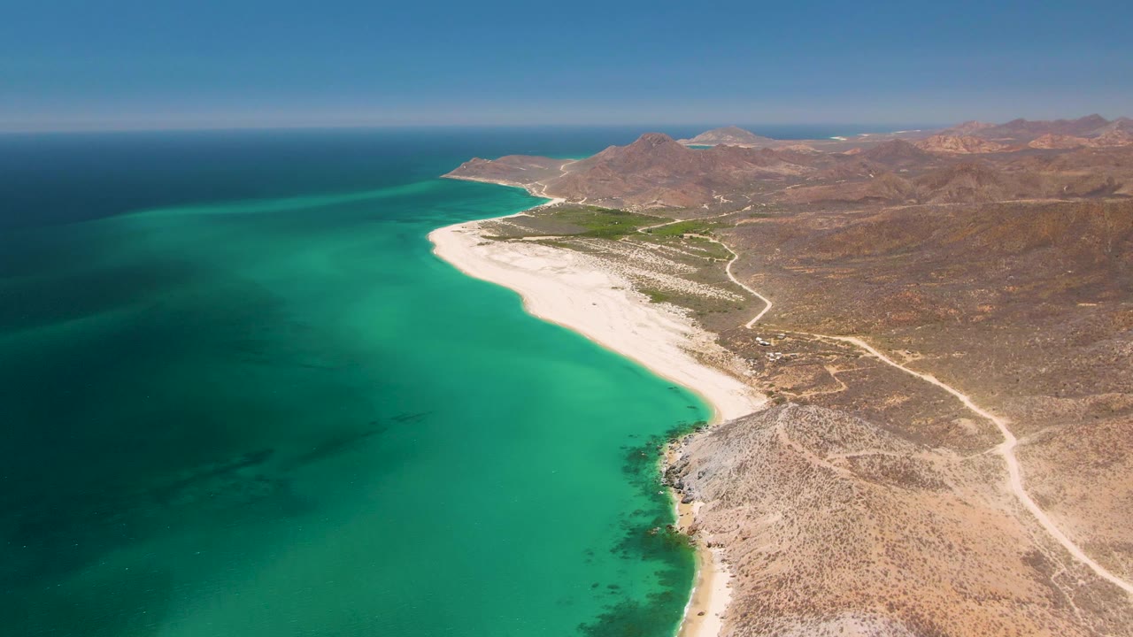 Fourth frame shows Playa Miramar Los Cabos from above, with darker teal water in the lower left, bright turquoise shallows near shore, a white beach, inland tracks, brown mountains, and no visible people.