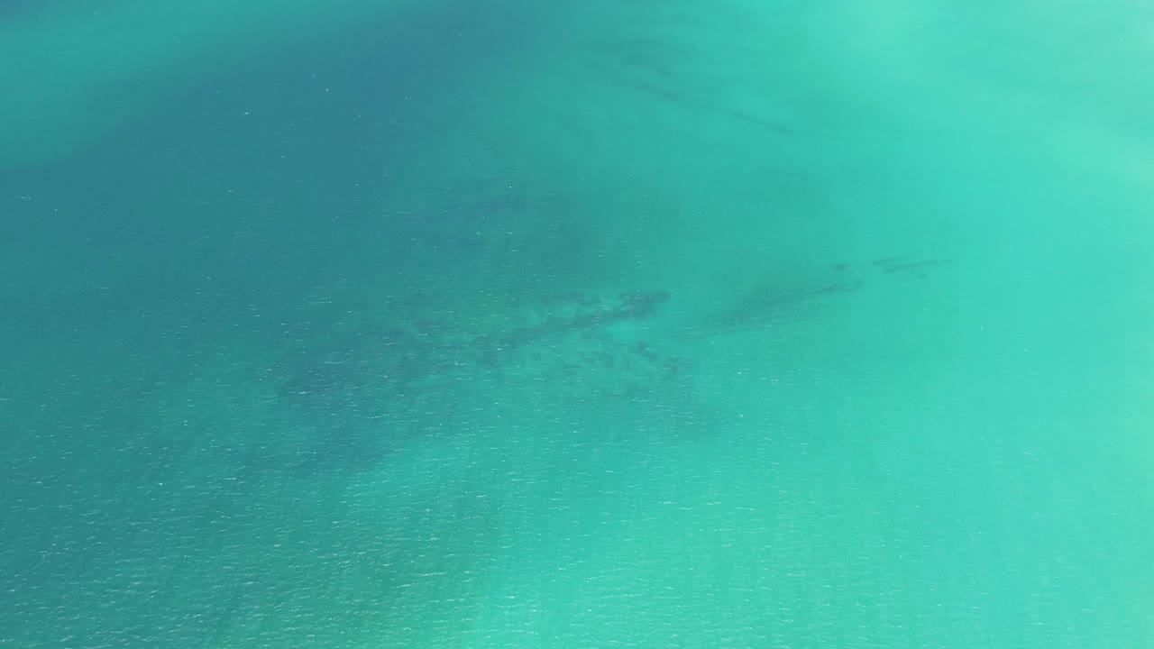 Teal and turquoise water fills the frame at Playa Miramar Los Cabos, with faint seabed texture and no visible people.