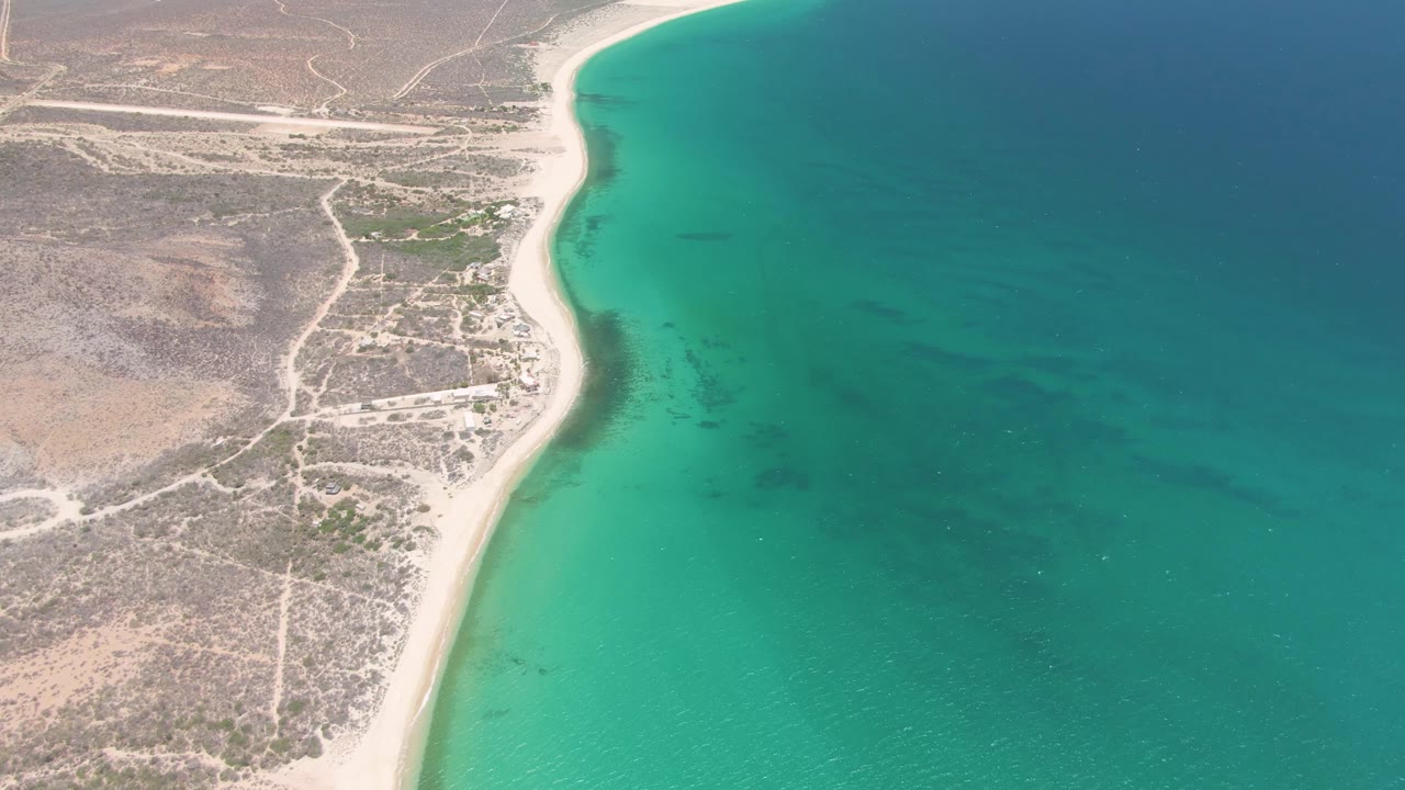 Aerial view of sandy shoreline beside turquoise ocean and dry inland roads.