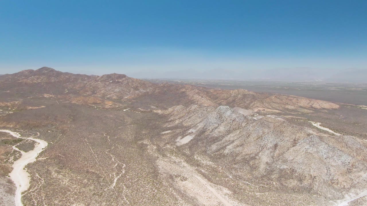 Wide aerial view over rocky desert terrain and distant mountains.
