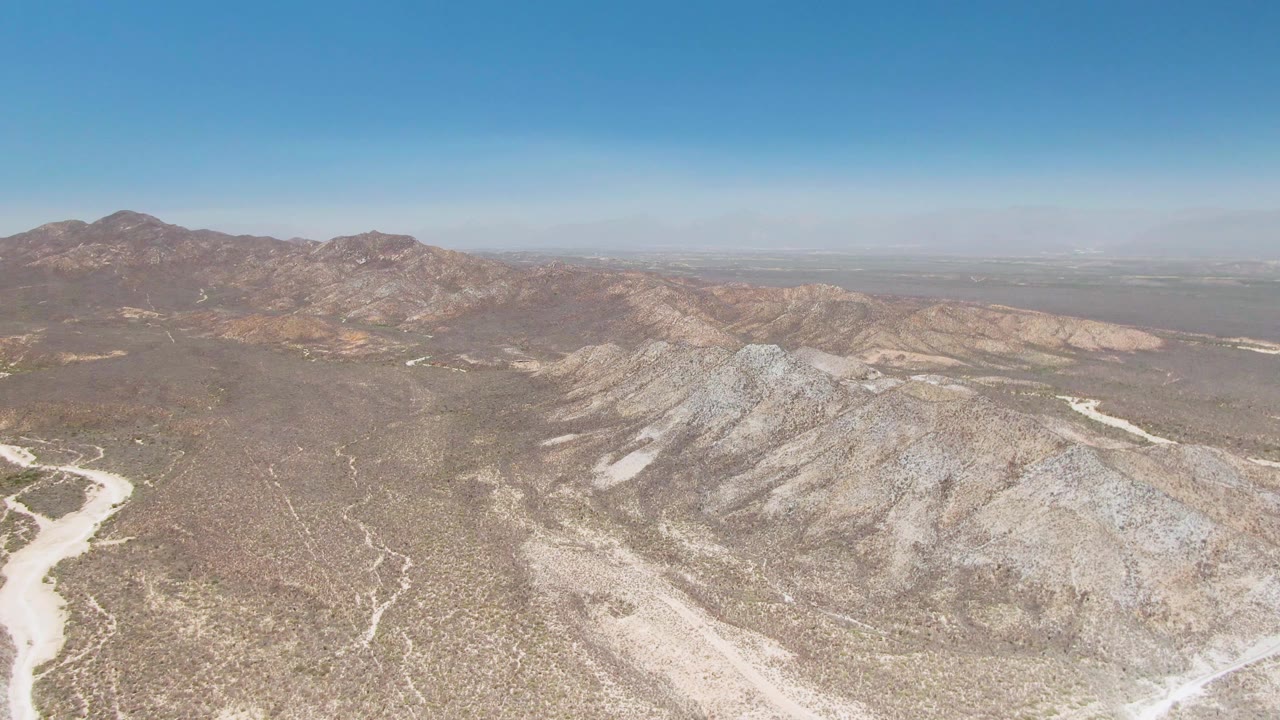High desert aerial with pale wash cutting through rocky valley