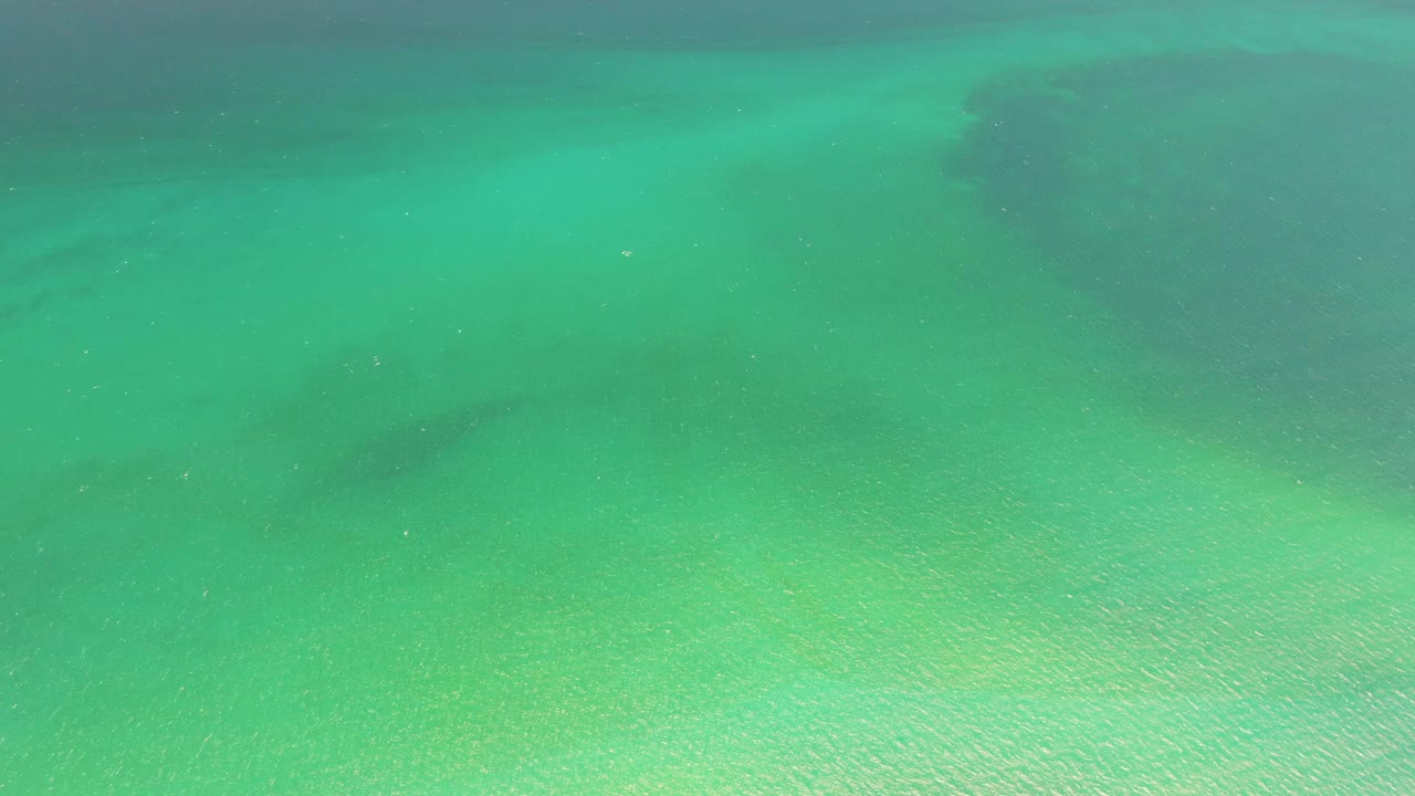 Clear green-blue water with sand texture visible below.
