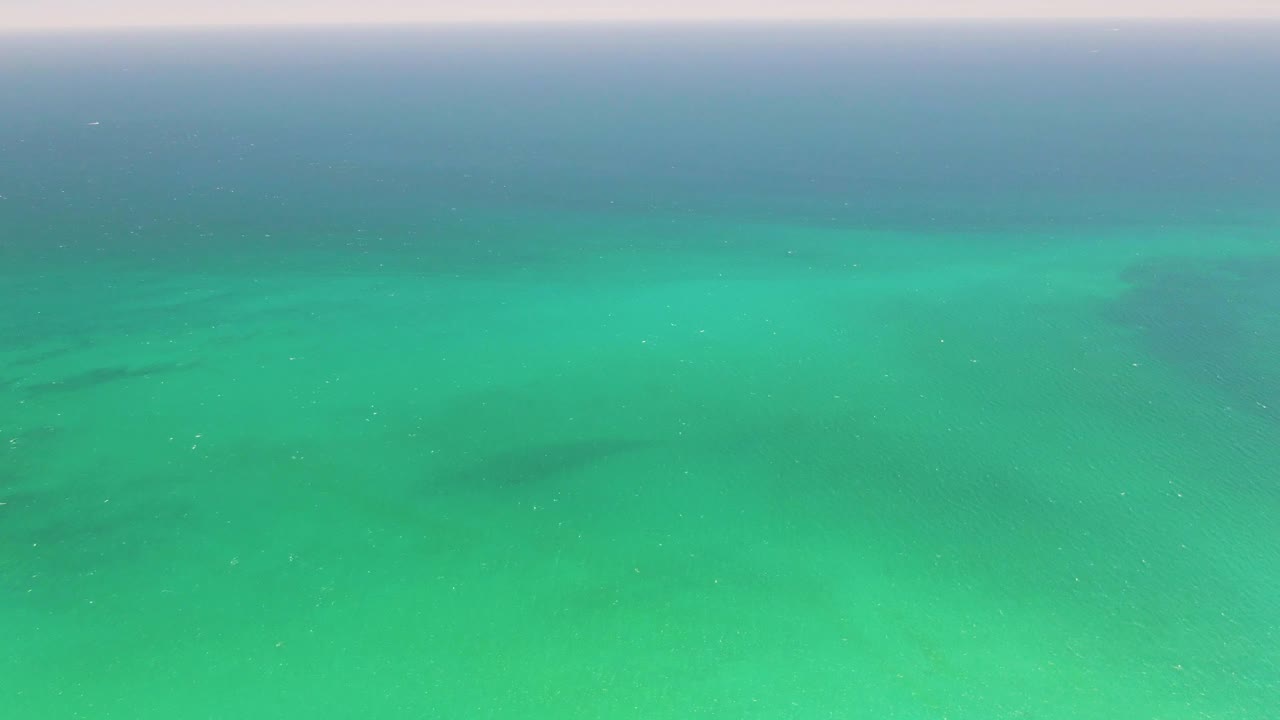 Mid-clip frame from Playa Miramar Los Cabos with turquoise shallow water filling the view, darker seabed features beneath, and no visible people or vessels.