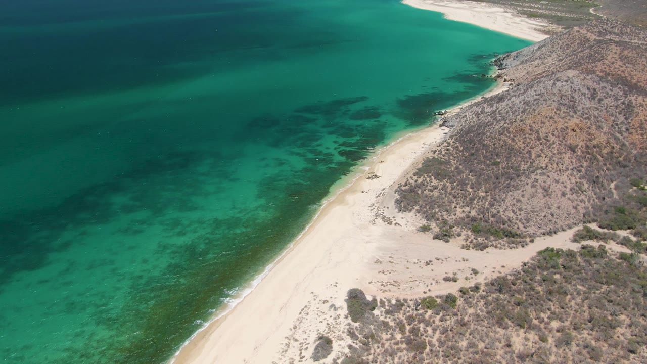 Aerial view of turquoise ocean beside a sandy beach and rocky hillside