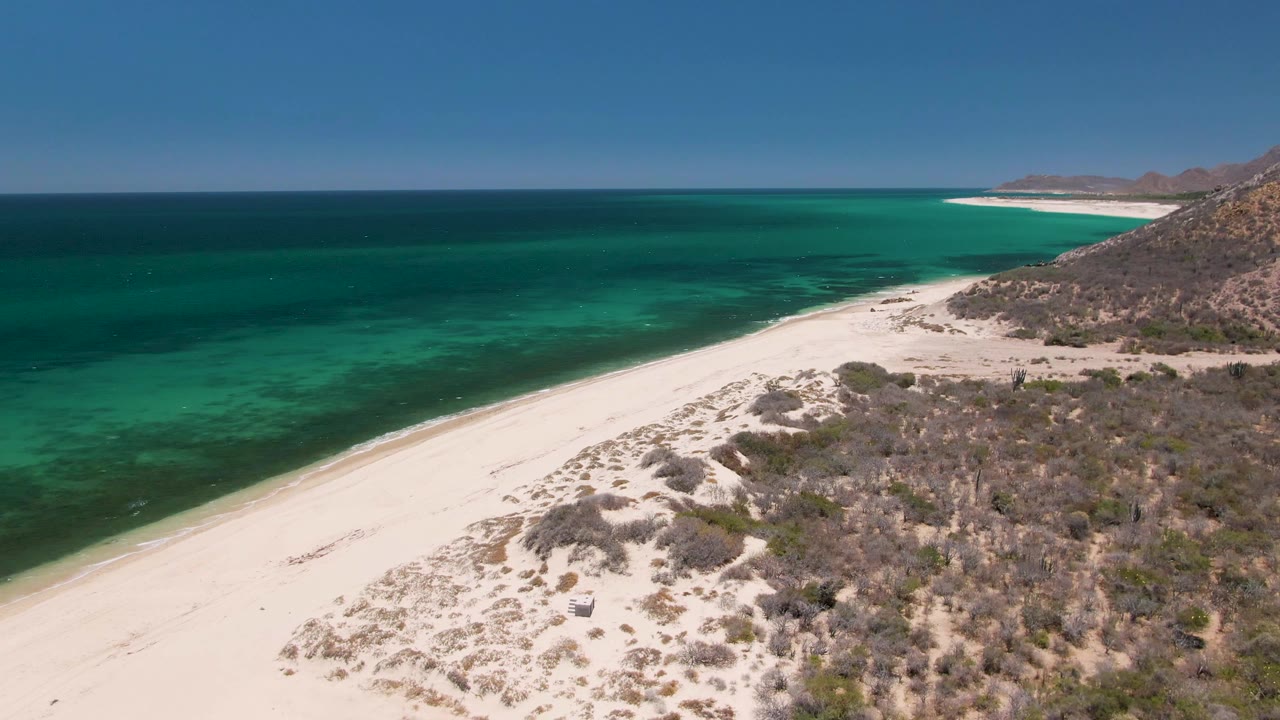 Aerial view of white sand beach beside turquoise ocean and dry scrubland.