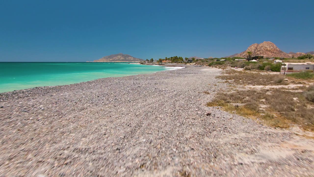 Aerial view of turquoise water meeting a wide pebbled shoreline.