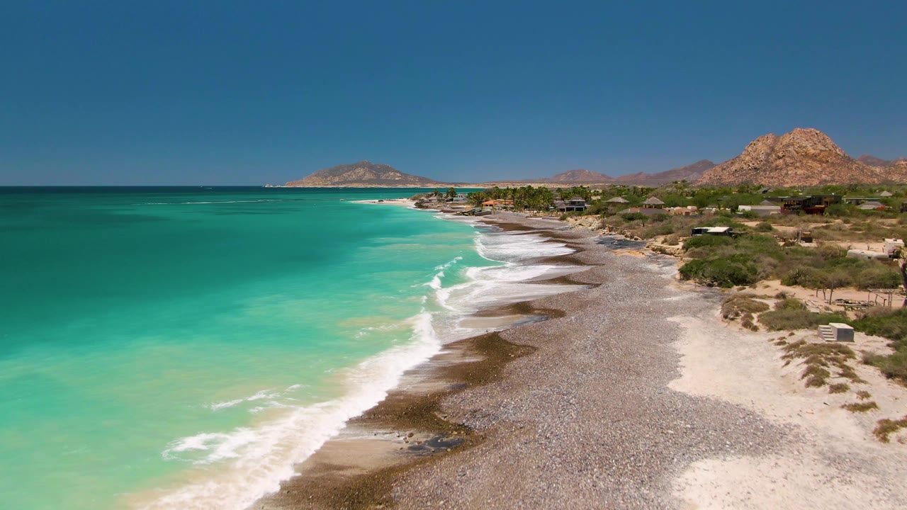 High coastal view of clear water and a pebbled beach below arid hills.