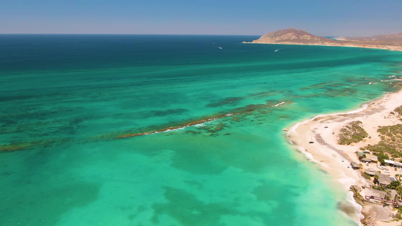 Aerial shoreline with deeper blue ocean beyond turquoise shallows and a sandy beach.