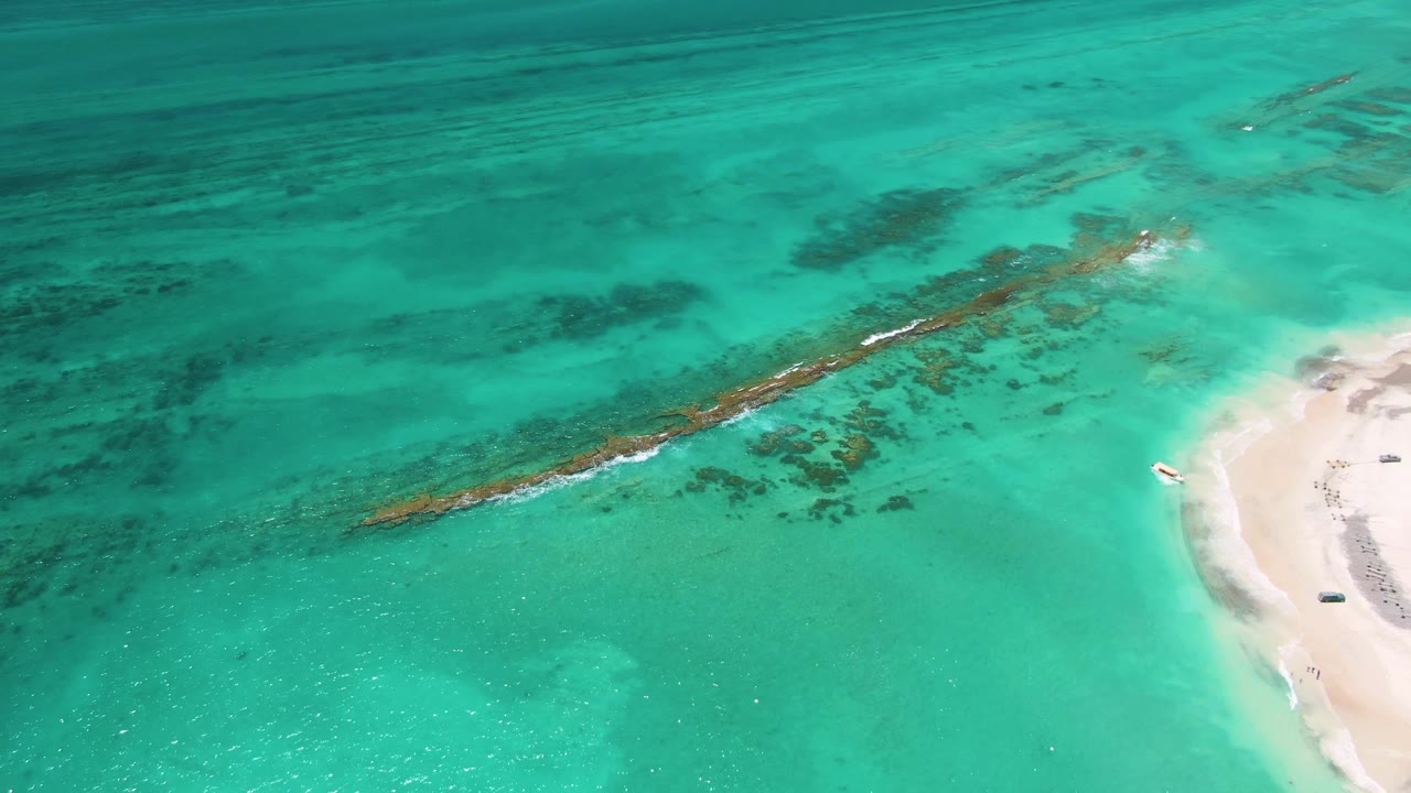 A white wave line begins to stretch along the diagonal reef under clear turquoise water near the Cabo Pulmo shoreline, with no visible people.