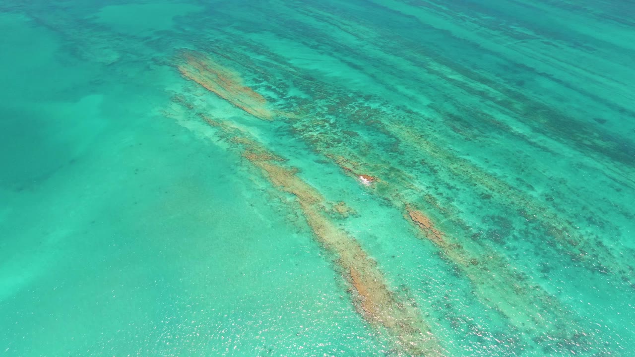 Aerial frame in Cabo Pulmo showing blue-green water over elongated submerged formations, with the red buoy slightly lower in the composition and no visible people.