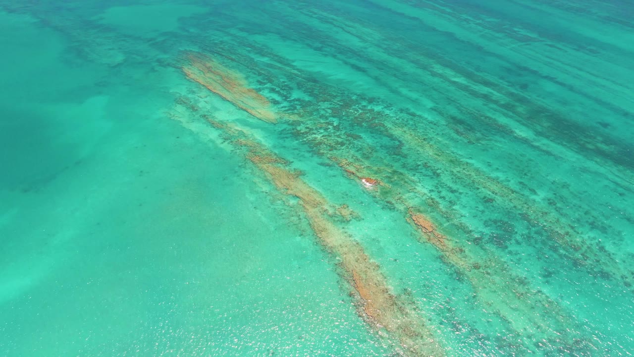 Overhead Cabo Pulmo view with turquoise water, diagonal shallow submerged structures, darker bands of water near the upper frame, and no visible people.