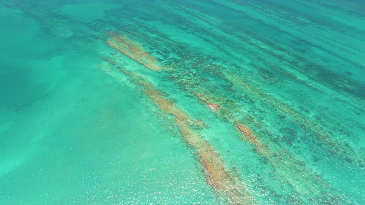 Shallow turquoise water with submerged formations and a red buoy near the lower middle.