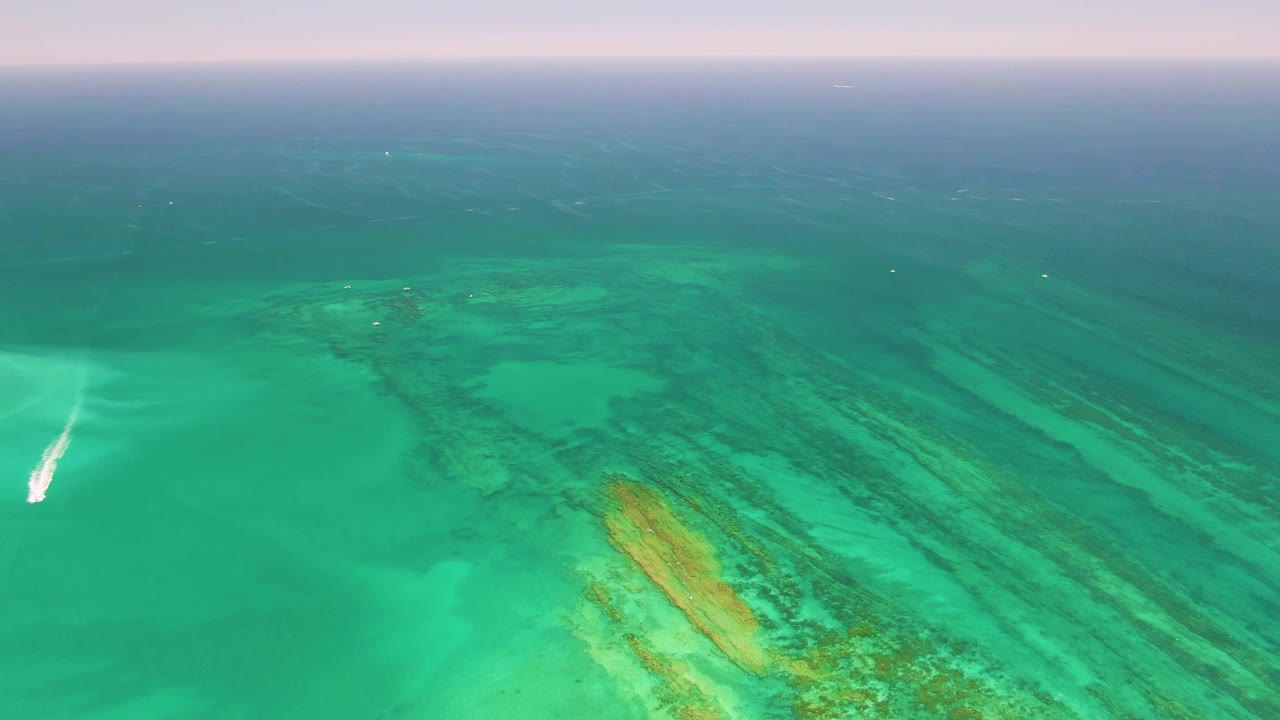 Aerial view of turquoise reef water with a small boat wake at the left edge.