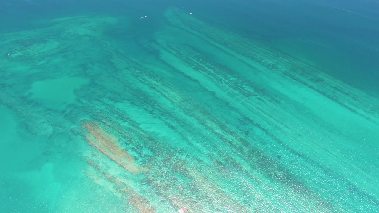 At 0:01, the Cabo Pulmo aerial view holds over clear blue-green water, with long dark reef lines crossing the sandy seabed and no visible people.