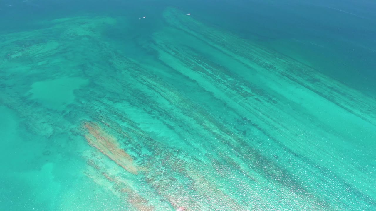 At 0:02, the Cabo Pulmo reef fills the frame with turquoise shallows, dark seabed streaks, a pale sand channel, and no visible people.