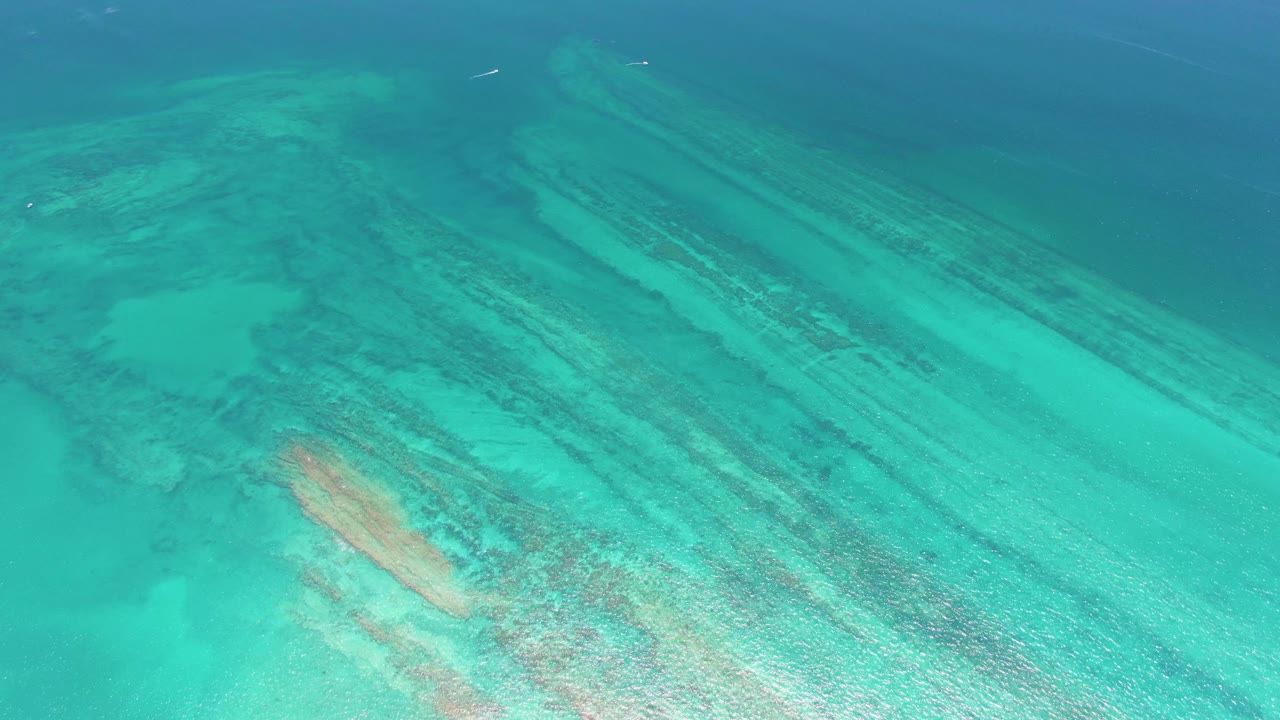 Overhead frame of blue-green water revealing long coral reef bands and sandy seabed in Cabo Pulmo, Mexico, with no visible people.