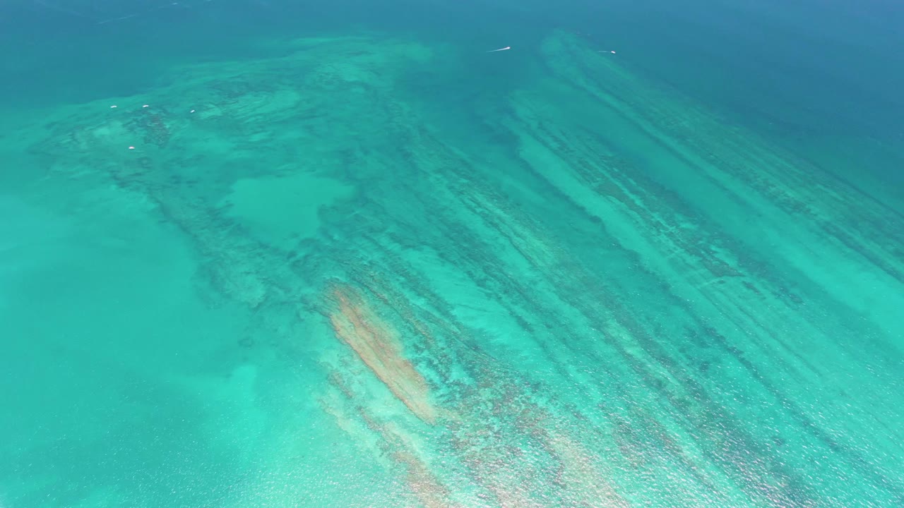 Aerial view of turquoise shallow water over dark coral reef bands and a pale sand patch in Cabo Pulmo, Baja California Sur, with no visible people.