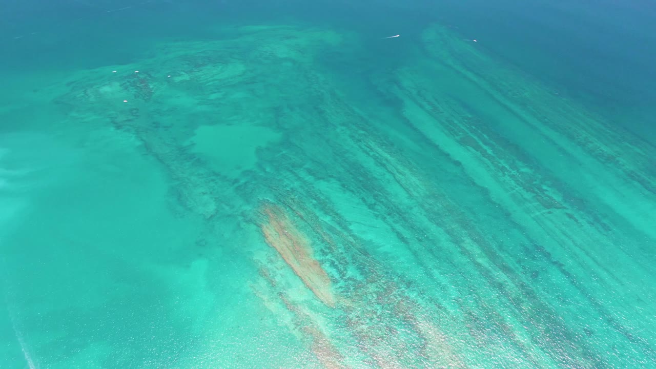 Aerial frame of clear blue-green water in Cabo Pulmo with long submerged reef ridges running diagonally and no visible people.