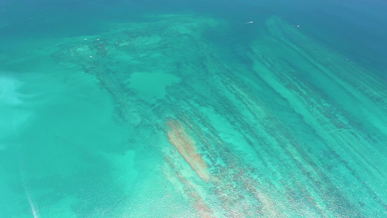 Overhead view of Cabo Pulmo shallow sea with a pale sand formation near the lower frame and darker coral patches visible through the turquoise water, with no visible people.