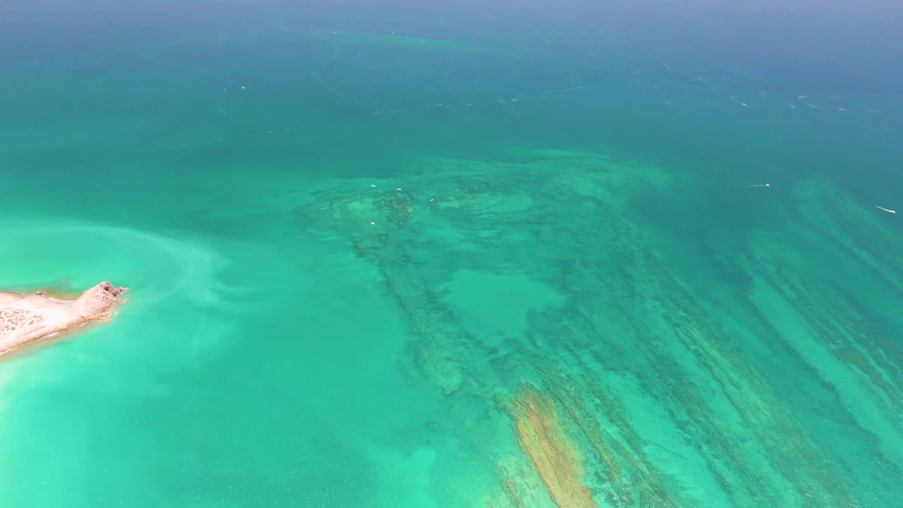 At two seconds, the small sand point remains on the left of the Cabo Pulmo frame, with green-blue shallows and darker coral textures visible beneath the surface, and no visible people.