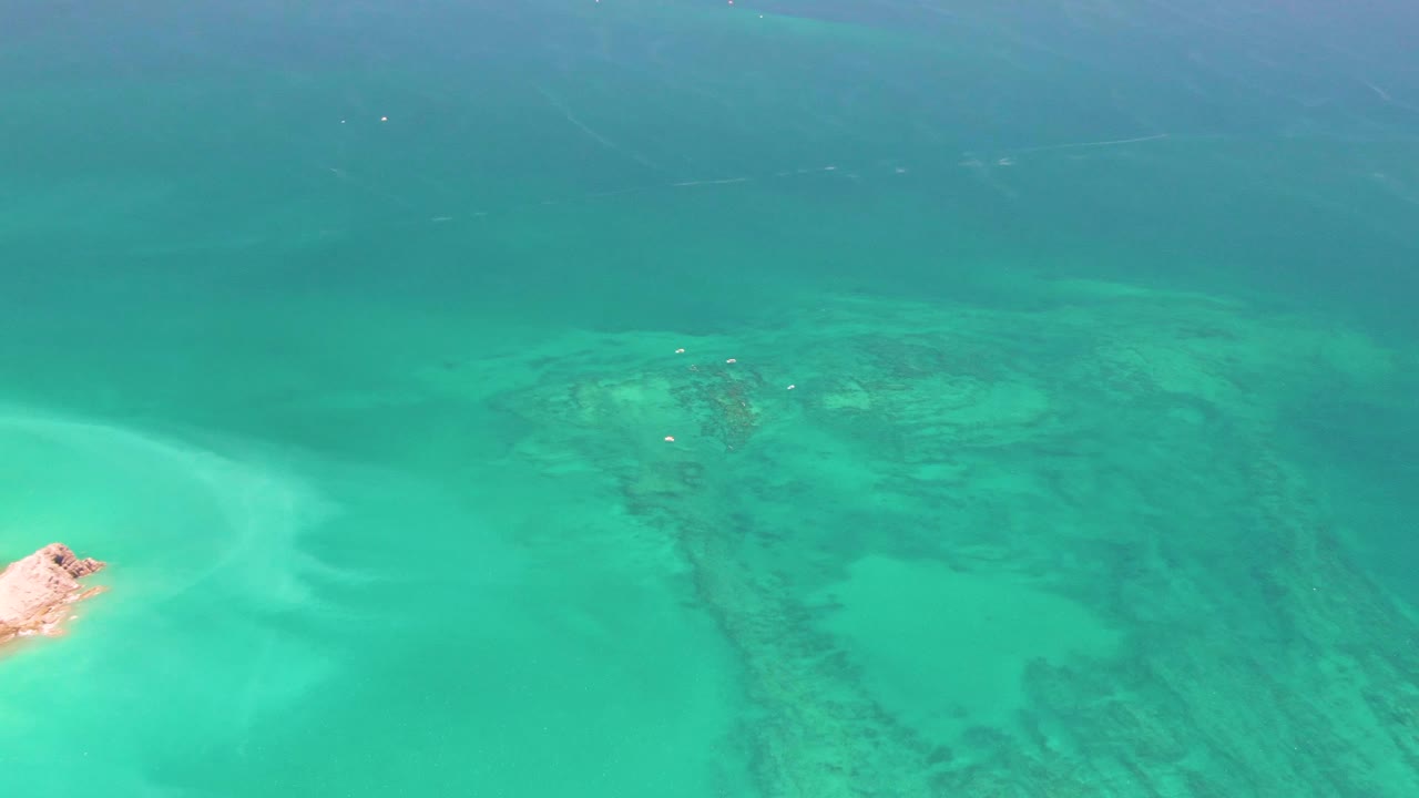 Aerial ocean view with a cropped rocky edge, pale shallows, and darker underwater patches.