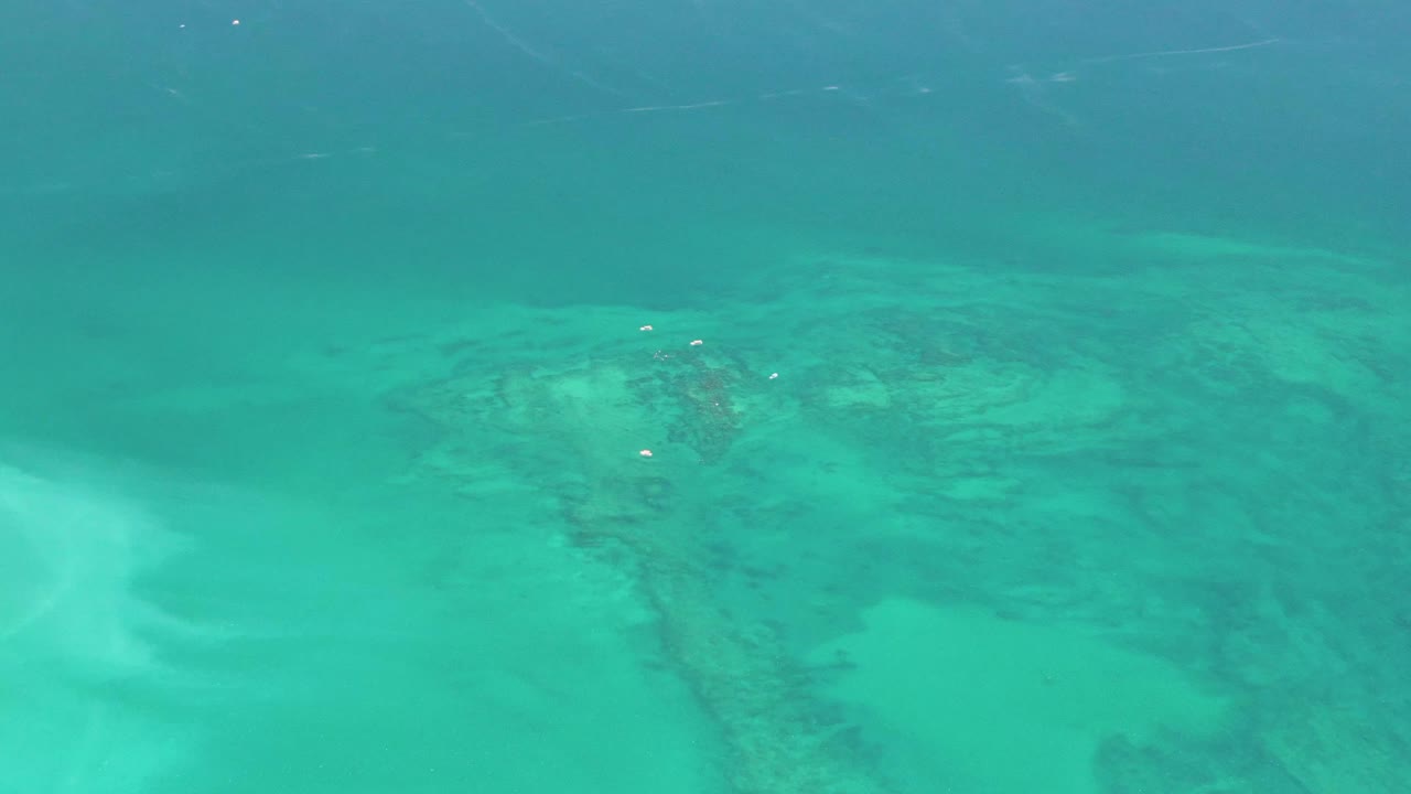 Clear turquoise water in Cabo Pulmo shows pale sandy shallows and darker submerged reef or rock patches, with no visible people in this opening frame.