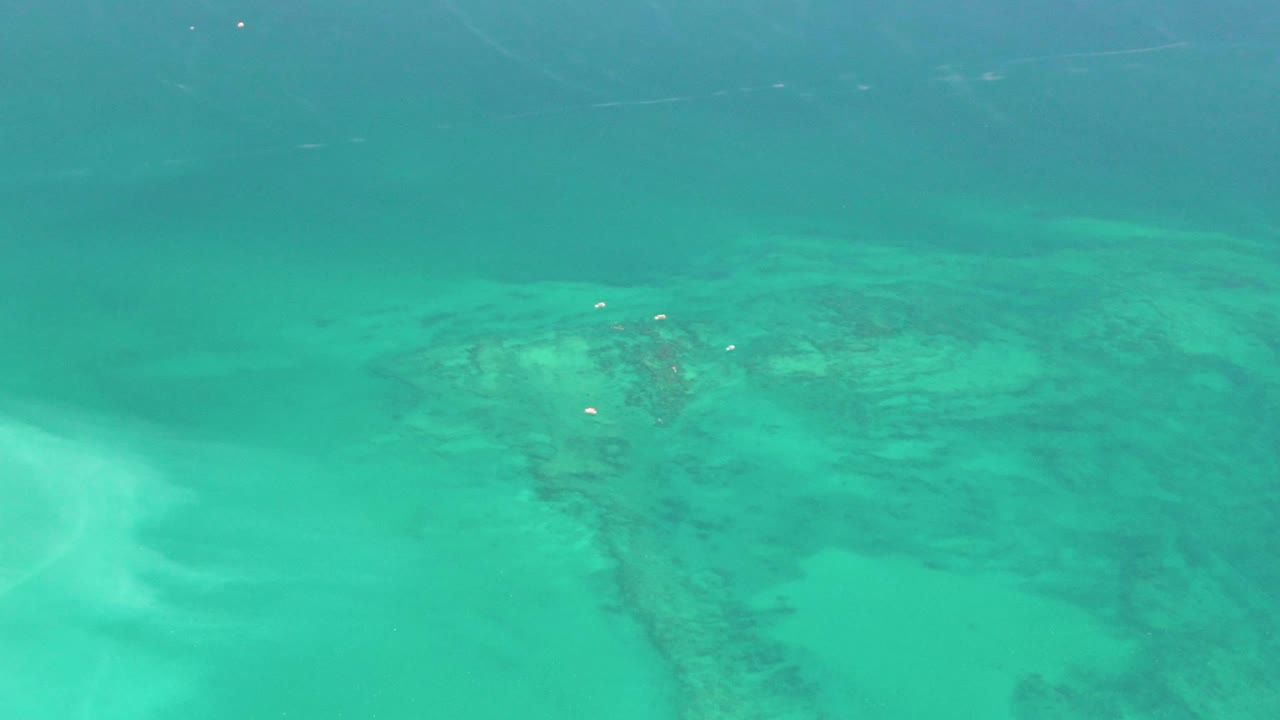 At one second, the frame holds on blue-green water over pale sand and irregular darker seabed forms in Cabo Pulmo, with no visible people.