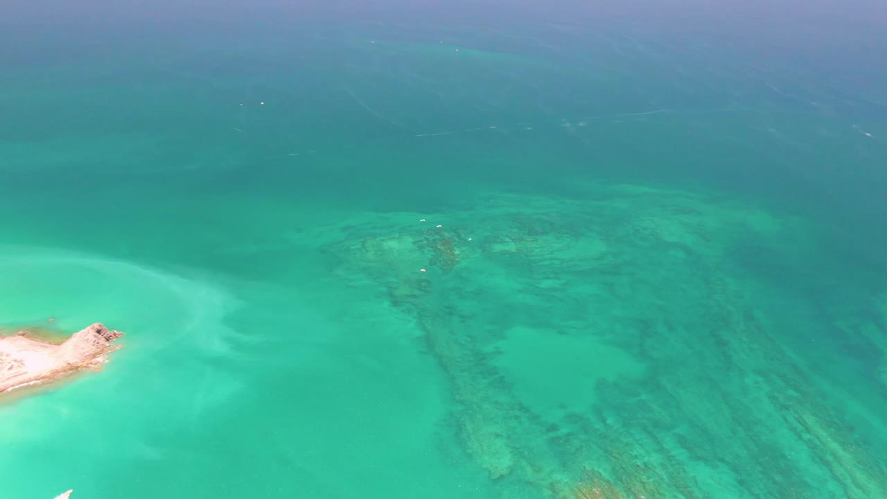 Aerial view of a small sand island beside turquoise water and reef patterns.