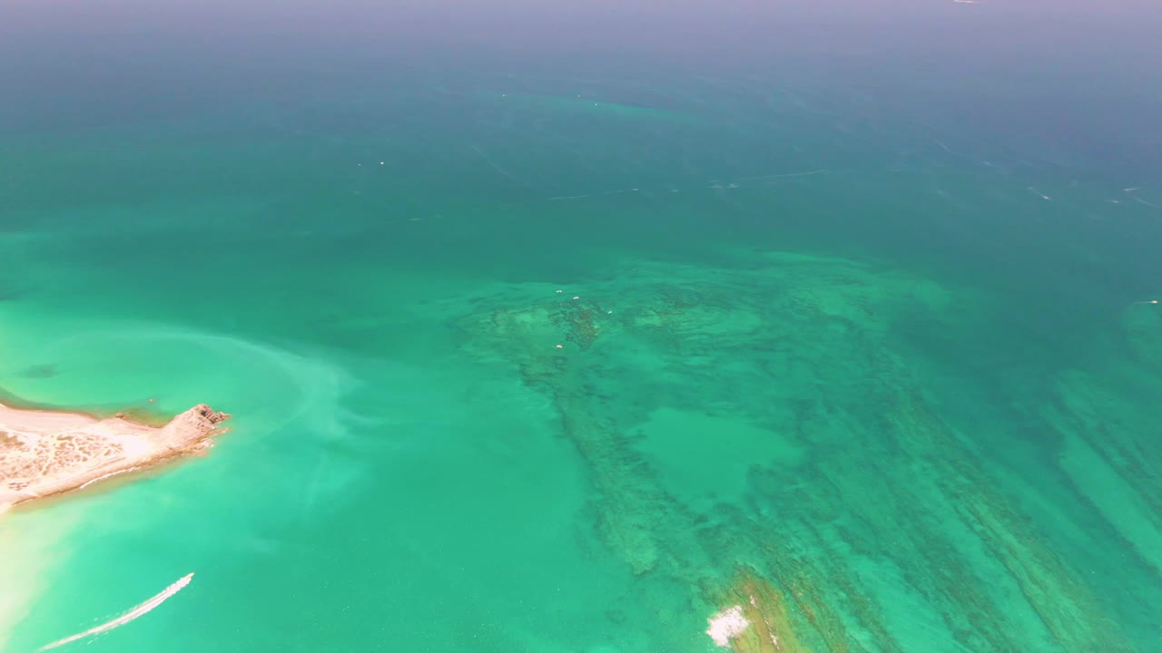 Aerial frame from Cabo Pulmo, Mexico showing the boat wake farther into the lower left water, the sand island cropped at left, darker reef patches at right, and no visible people.